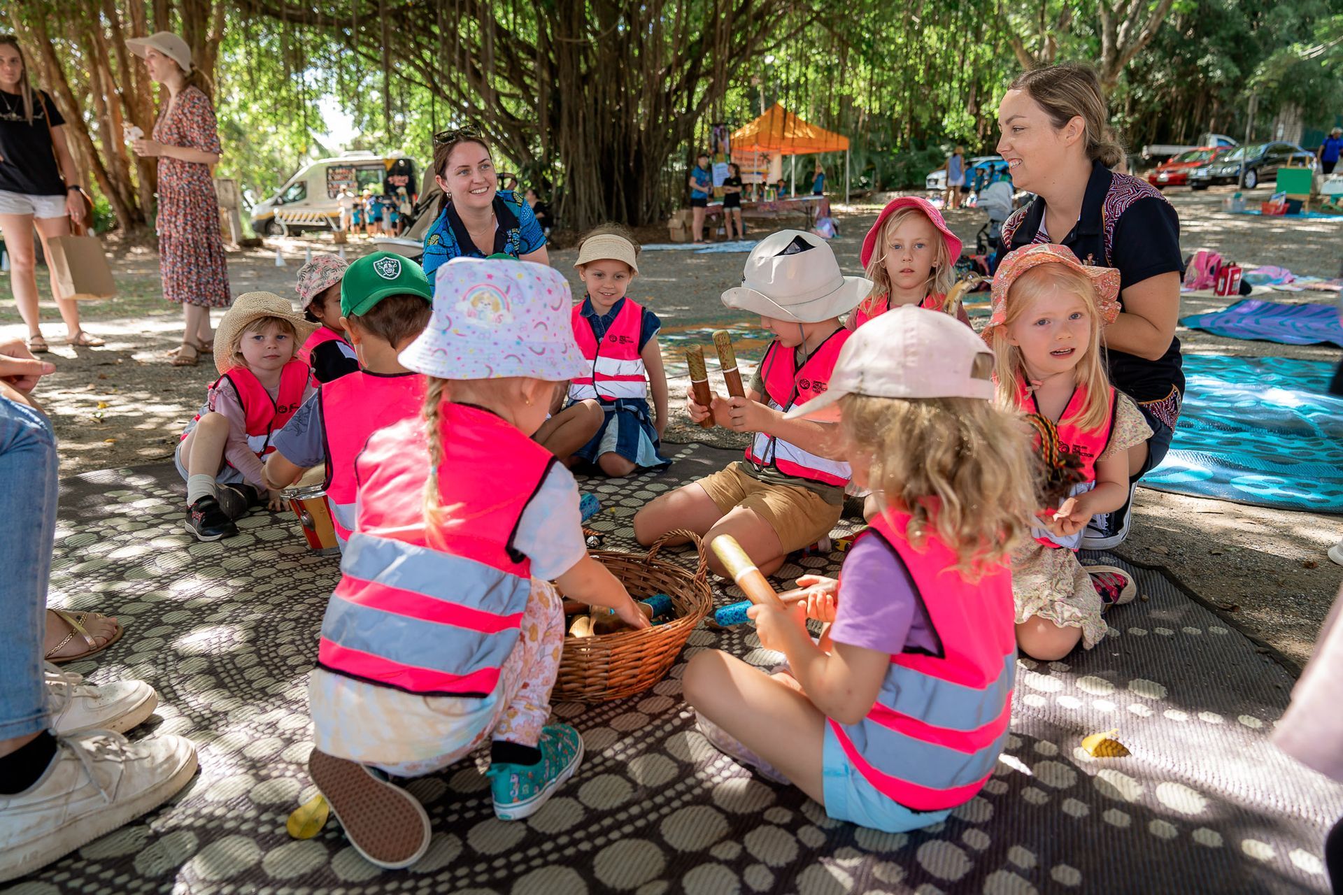 A group of children are sitting on a blanket under a tree.