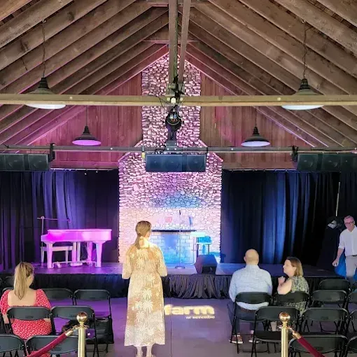 An indoor performance space with a stage, piano, and audience seated in chairs.
