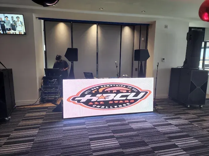 DJ setup with LED sign for H-BCU Conference. Includes speakers, equipment, and a DJ in a room.