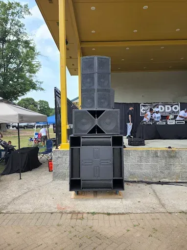 Large black speaker system stacked on a stage with people in the background.