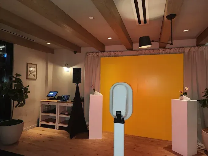 Photo booth setup with yellow backdrop, speaker, and white pedestals in a room with wooden beams.