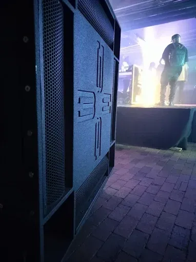 Large black speaker cabinet near stage with performer illuminated by light.