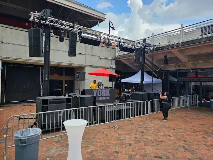 Outdoor event setup with stage, DJ, sound equipment, and crowd barriers.