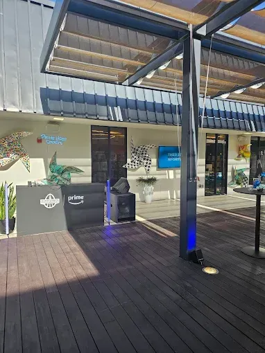 Outdoor deck with a DJ setup in front of a building with windows, under a shaded structure.