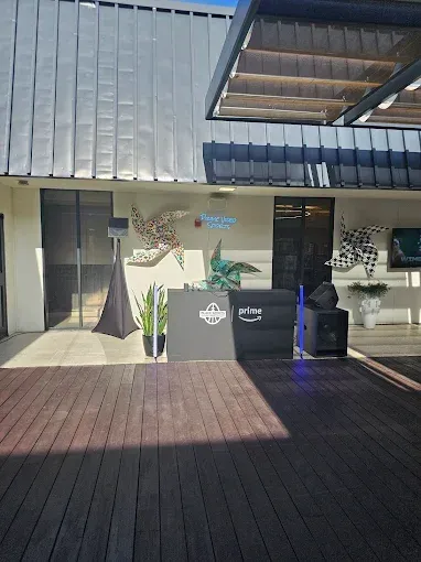 DJ setup on a wooden patio; venue exterior. Black DJ booth, speakers, plants, and art.