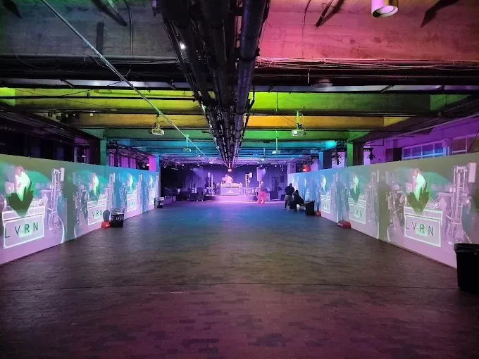 Large indoor space with projected images on walls, stage, and colorful lighting.