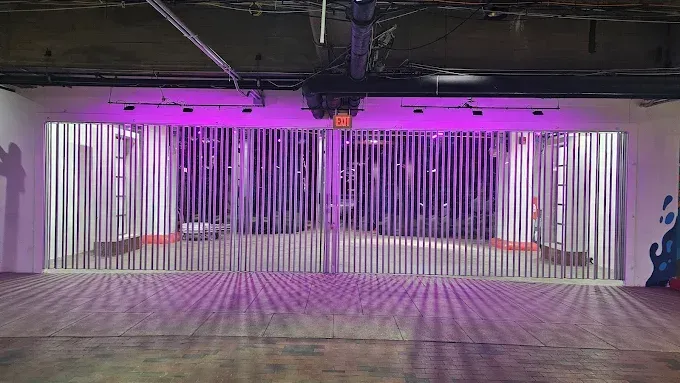 Open room with vertical metal rods, lit in purple, casting shadows.