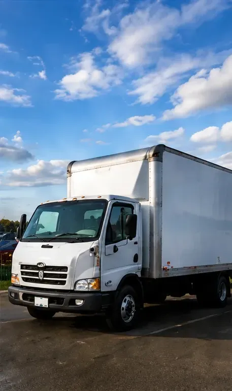White box truck parked on wet pavement under a partly cloudy blue sky.