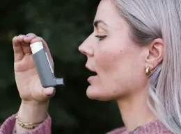 A woman in a blue sweater is blowing her nose into a napkin.