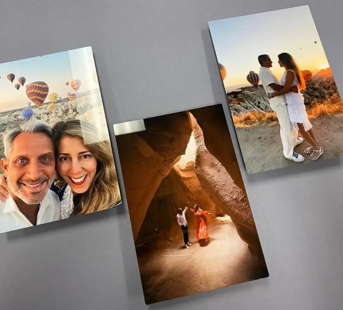Three printed travel photos on a gray surface: a smiling couple, a canyon scene, and a backlit couple at sunset