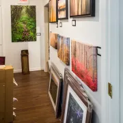 Hallway gallery with colorful landscape paintings displayed on white walls and leaning along the floor