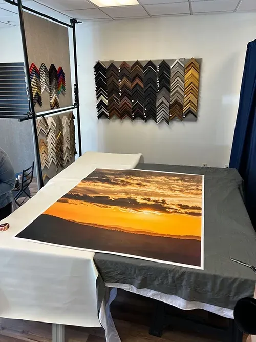 Framed sunset photo laid on a table in a frame shop with sample frames on the wall