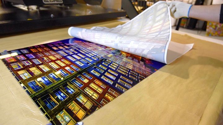 Colorful printed sheet being peeled back on a table, revealing a grid of bright images underneath