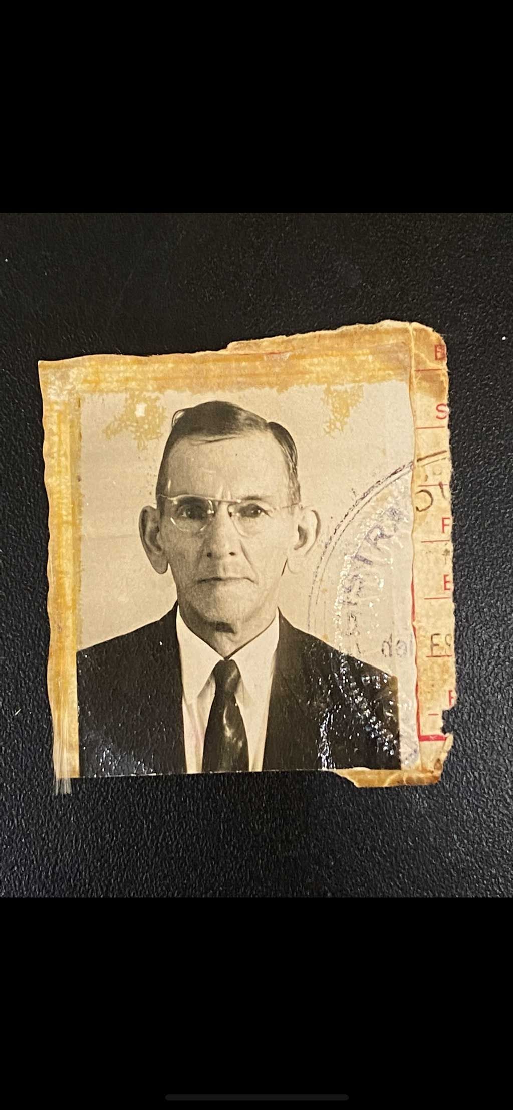 Small worn black-and-white portrait photo of a man in a suit and tie on a torn beige background