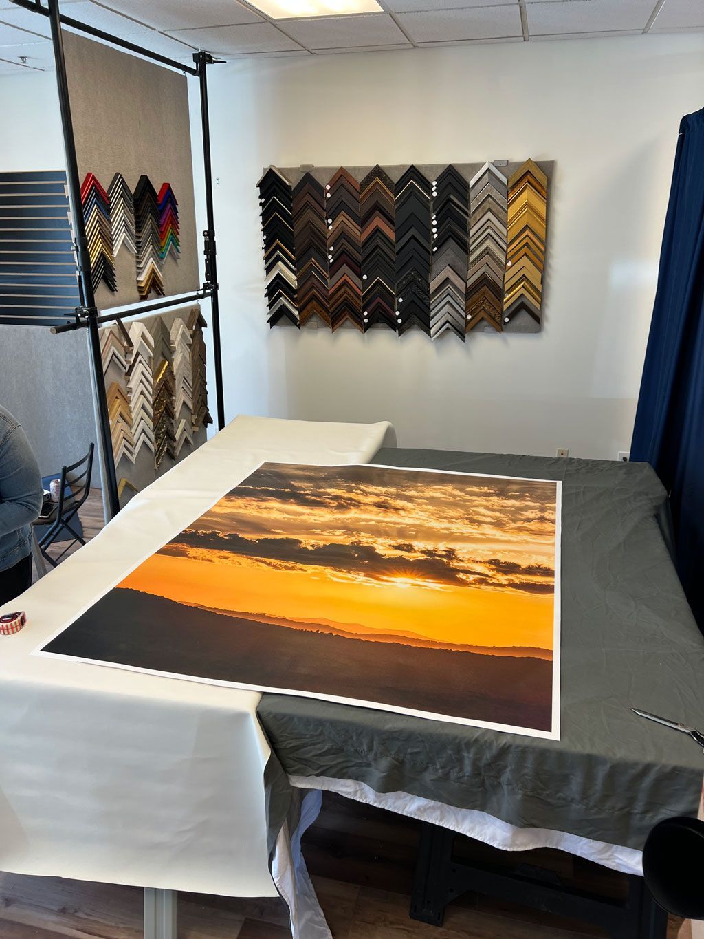Framed sunset print on a table in a framing shop, with frame samples displayed on the walls.