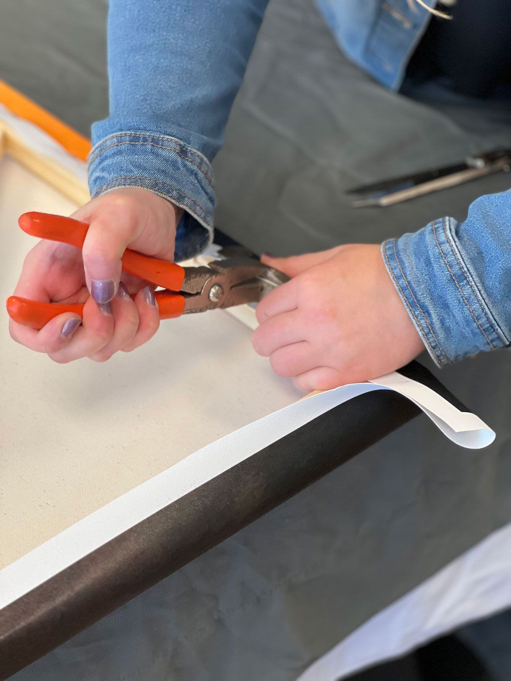 Hands using orange pliers to cut a white zip tie on a black bar