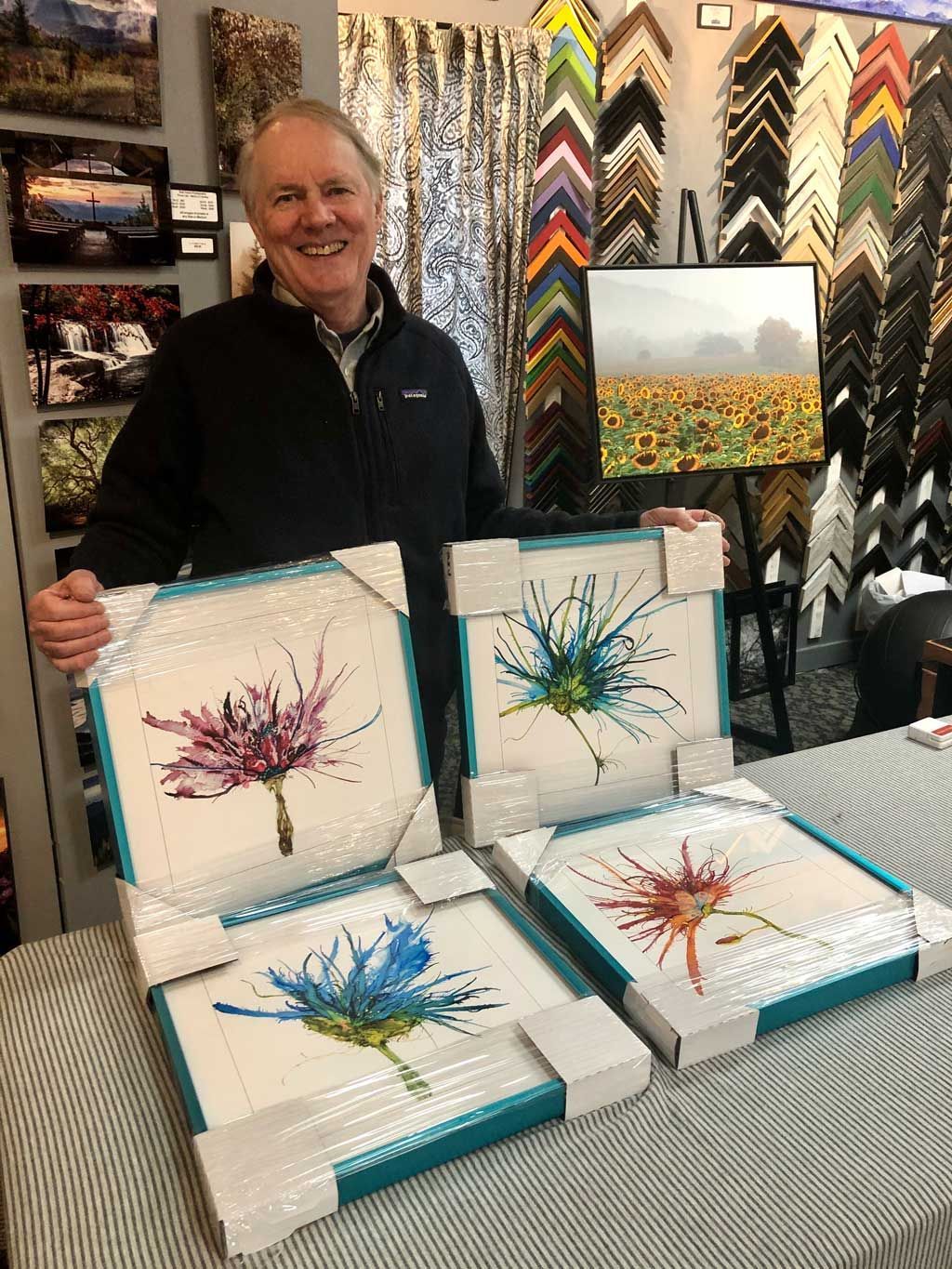 Artist smiling behind colorful abstract prints in a gallery booth