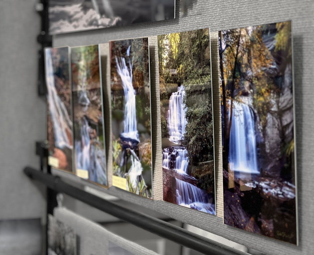 A row of framed waterfall photos displayed on a wall or shelf outdoors.