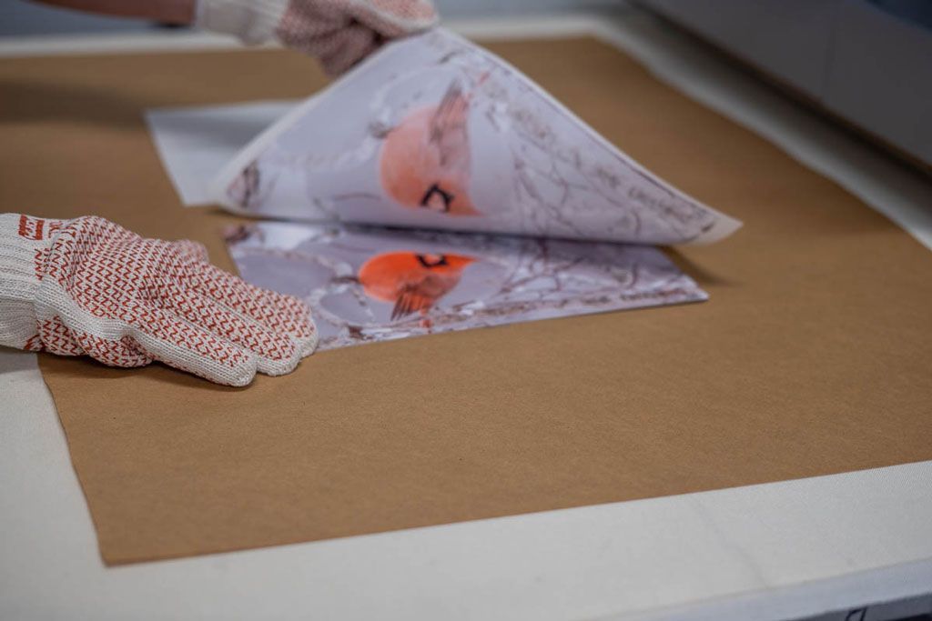 Hands folding patterned fabric over brown paper on a worktable