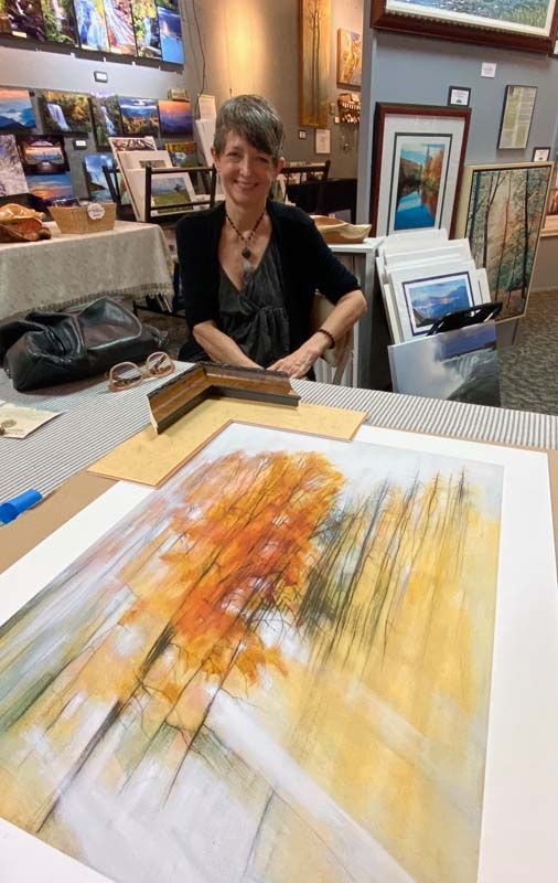 Artist smiling at a table beside colorful abstract paintings in a gallery studio.