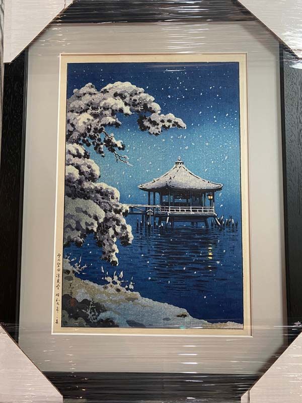 Framed winter painting of a snow-covered pavilion over dark blue water at night with a snowy tree in the foreground