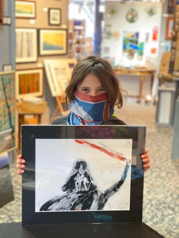 Person in a mask holding a framed black-and-white drawing in an art gallery