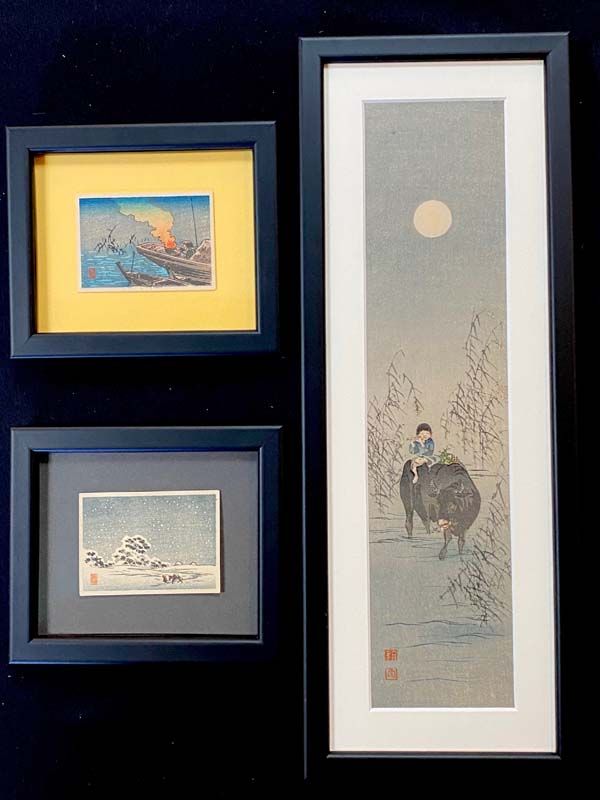 Three framed artworks on a dark wall, including a tall vertical print and two smaller landscape prints.