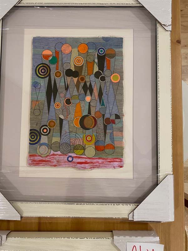 Framed abstract print with colorful circles, shapes, and vertical lines on a light wall