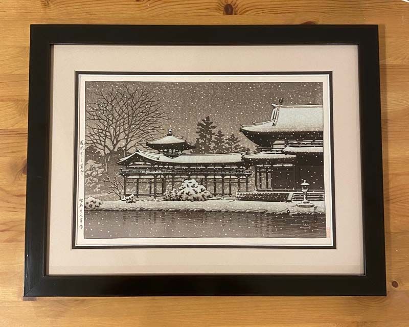 Framed black-and-white winter scene of a snowy temple or shrine on a wooden wall