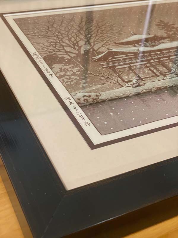 Framed winter landscape print with snow-covered trees and a dark frame on a tabletop