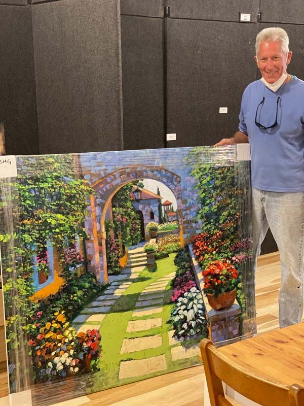 Man standing beside a colorful garden arch painting in a gallery room