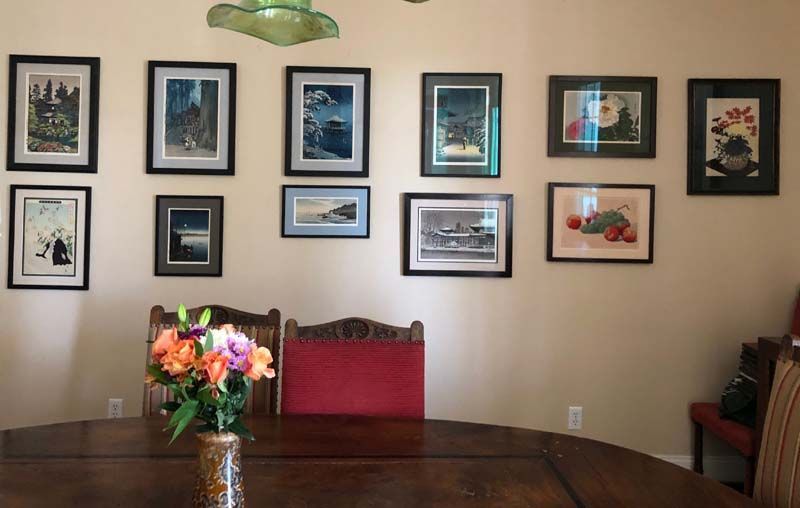 Dining room wall with framed artwork, a wooden table, and a vase of flowers in the foreground.