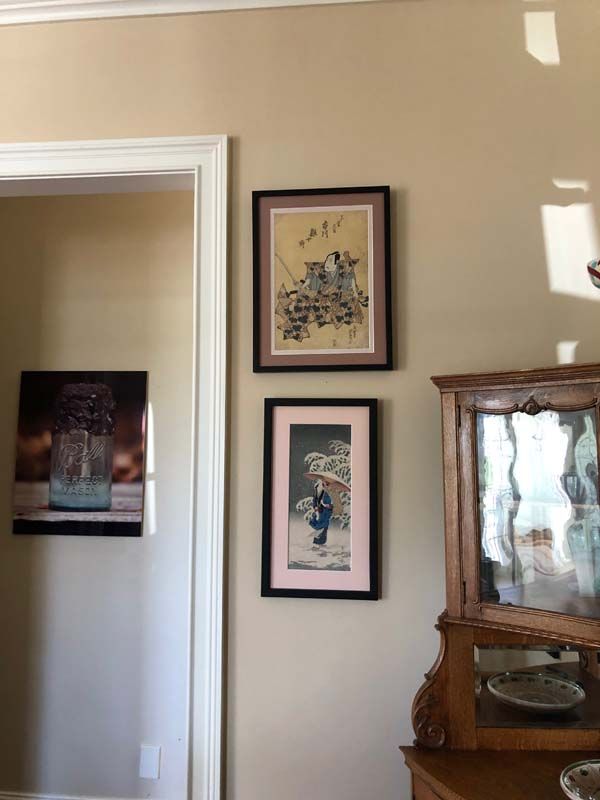Beige hallway wall with framed artwork beside a wooden glass-front cabinet.