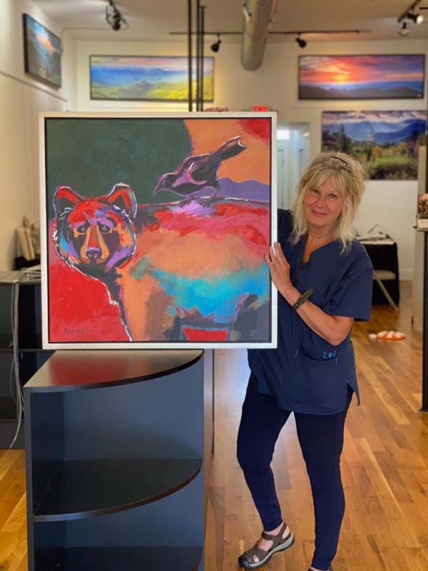Woman in blue scrubs holding a colorful horse painting in an art gallery