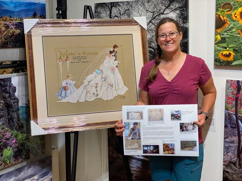 Woman in a pink shirt holding a display board beside a framed illustrated artwork at an art exhibit