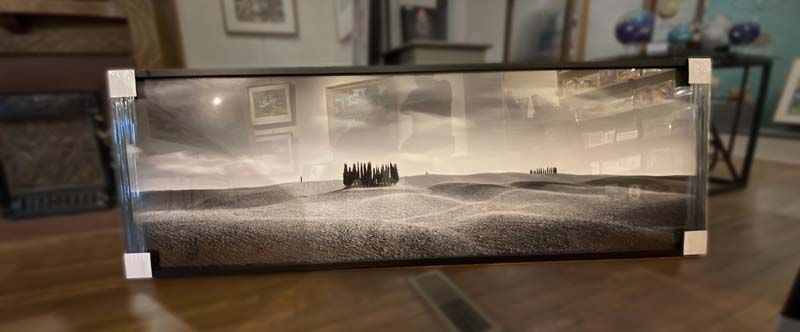 Panoramic black-and-white landscape print on a wooden table, with tiny figures in the distance.