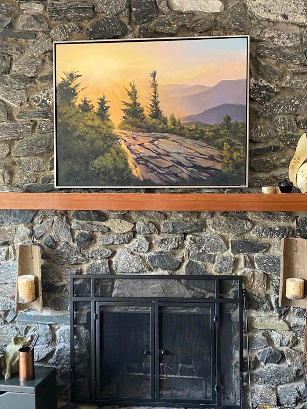 Stone fireplace with framed sunset landscape painting above the mantel.