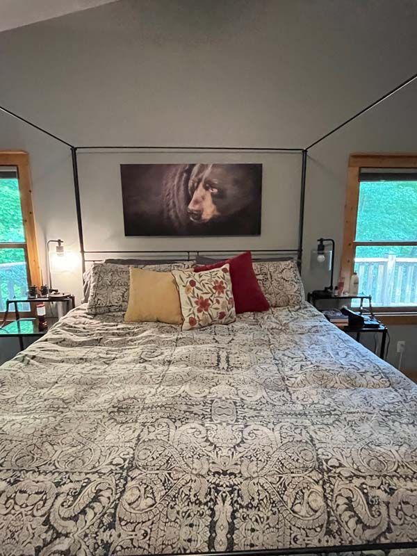 Bedroom with a large patterned bedspread, decorative pillows, and a framed wall art above the headboard.