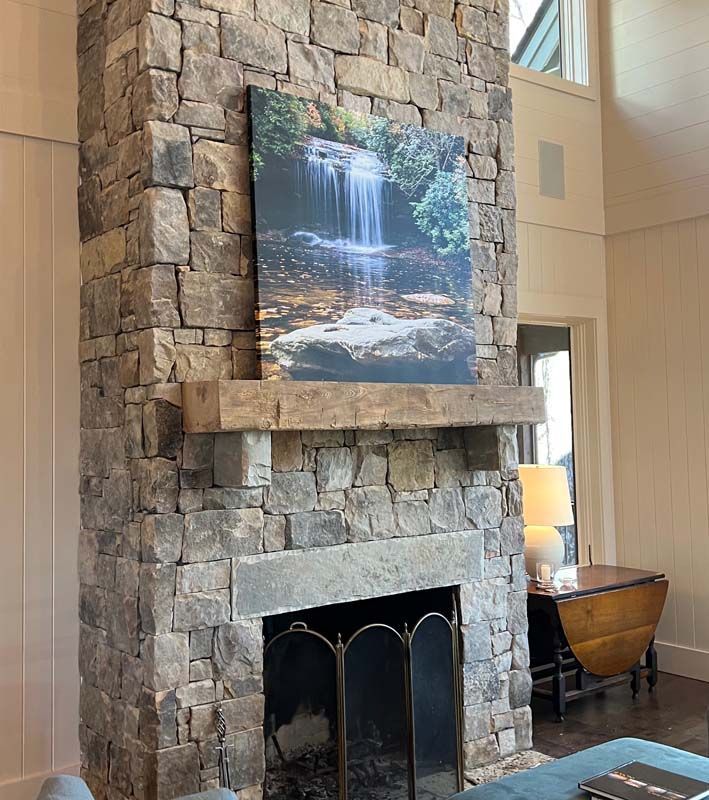 Stone fireplace in a bright room with a waterfall painting above the mantel.