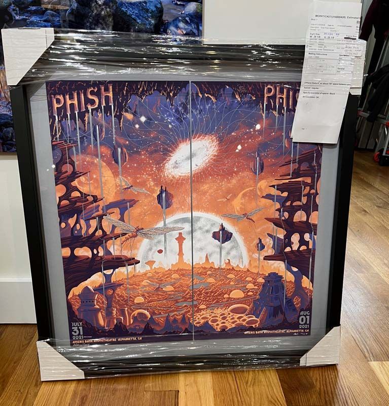 Framed Phish poster with a vivid orange sky and sci-fi landscape, on display in a store.