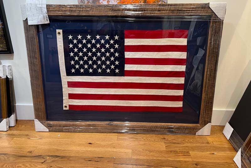 Framed American flag display leaning against a wall on a hardwood floor.