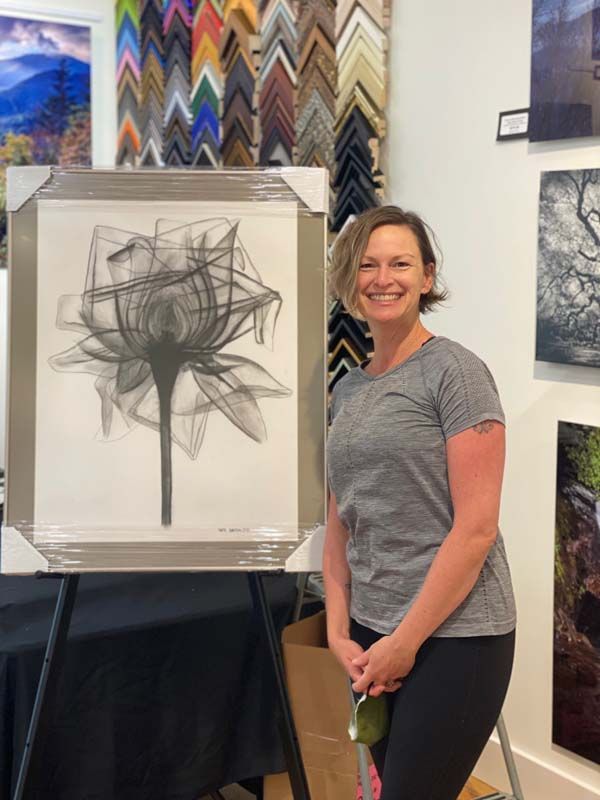 Woman smiles beside abstract charcoal artwork in a gallery.