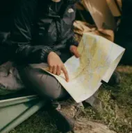 Person sitting in a tent, studying a folded map by flashlight at a campsite