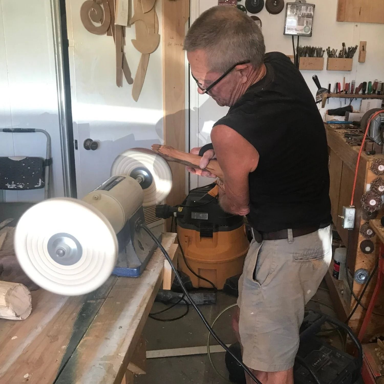 Man working on a wood lathe in a workshop, shaping a long cylindrical piece.