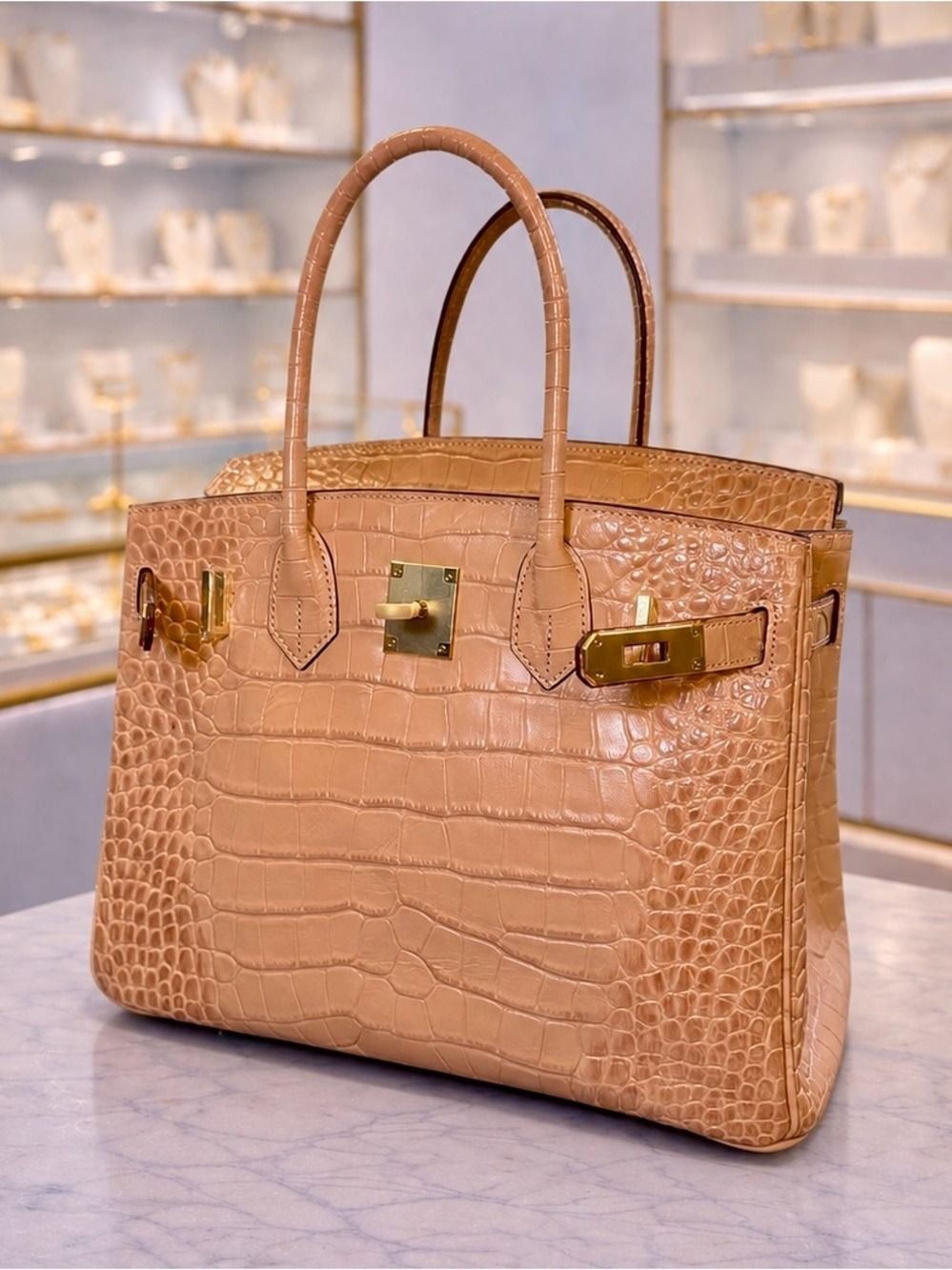 Tan crocodile-embossed handbag with gold hardware on a marble surface.