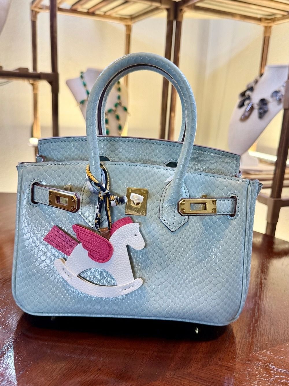 Light blue quilted handbag with charms on a wooden table outdoors