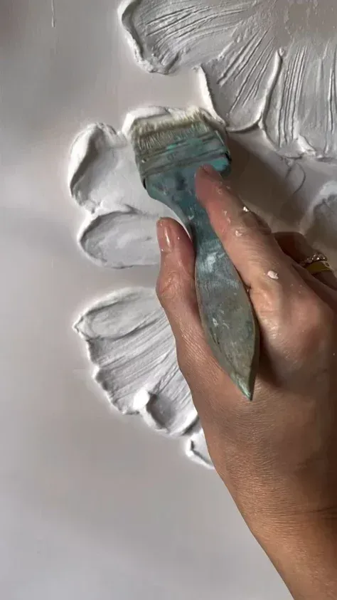 Hand spreading thick white plaster on a wall with a blue putty knife
