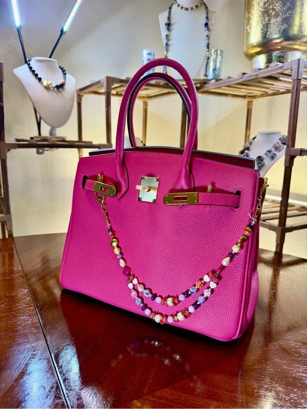 Pink handbag decorated with colorful beads on a wooden table, with jewelry displays in the background