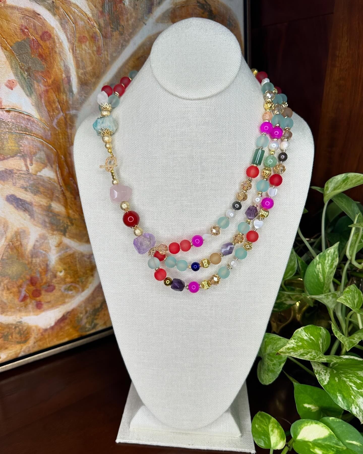 White necklace display bust with layered colorful beaded necklaces in pink, gold, blue, and red.