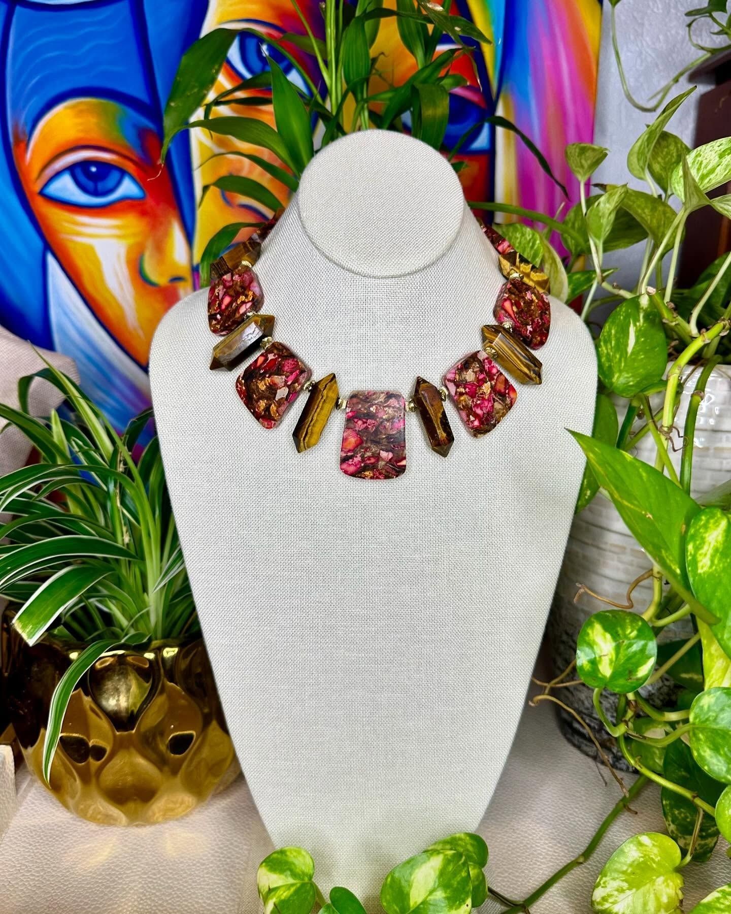 Jewelry display bust with a red gemstone necklace against a colorful painted background and green plants